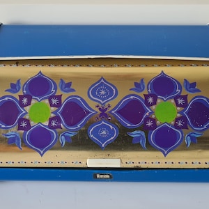 Puede incluir: Una panera vintage azul y dorada con un diseño floral decorativo en morado, verde y blanco. La panera tiene una parte superior curvada y un asa blanca. Mide aproximadamente 38 cm de largo.