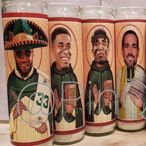 May include: Four glass candle holders featuring images of football players depicted in religious iconography. The candles are white and the images are colourful. The players are wearing green and gold uniforms. The candles are labelled with the number "33" and the words "Green Bay Defensive".