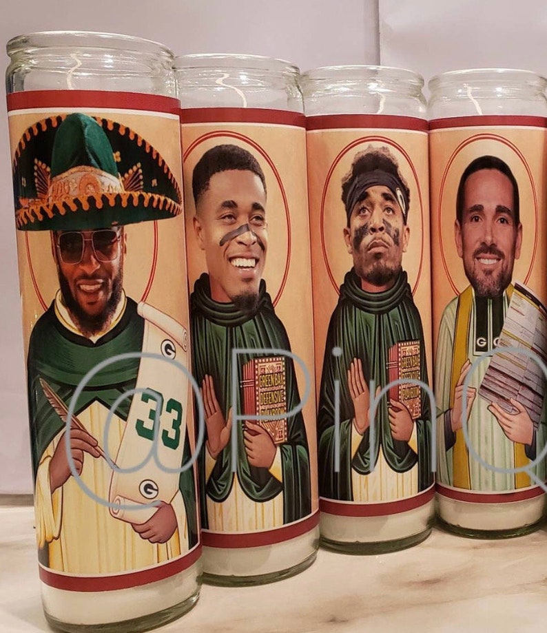 May include: Four glass candle holders featuring images of football players depicted in religious iconography. The candles are white and the images are colourful. The players are wearing green and gold uniforms. The candles are labelled with the number "33" and the words "Green Bay Defensive".