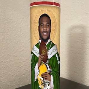 May include: A glass candle with a portrait of a football player, Micah Parsons, holding a football and a helmet. The candle has a green and gold color scheme, with the player's name on the jersey. The background is a decorative gold pattern.