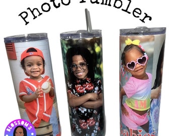 May include: Three stainless steel tumblers with personalized photos of children. The tumblers are white with a black base and feature a straw.