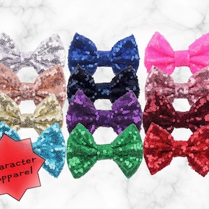 May include: Assortment of 10 sequined hair bows in various colors, including silver, pink, red, blue, green, and gold. The bows are arranged in two rows, with the top row slightly overlapping the bottom row. The bows are all made of the same material and have a similar shape.
