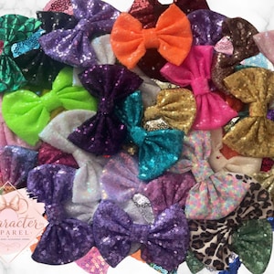 Puede incluir: Una colecci&oacute;n de lazos para el pelo variados con diversos colores y texturas, incluyendo lentejuelas, purpurina y estampados de animales. Un logotipo rosa claro en forma de diamante con el texto Character Apparel es visible en la esquina.