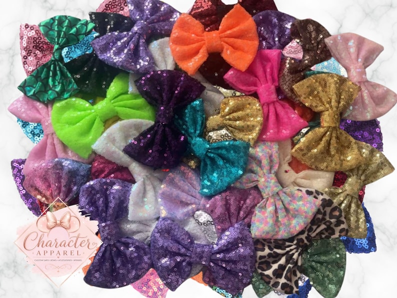 Puede incluir: Una colecci&oacute;n de lazos para el pelo variados con diversos colores y texturas, incluyendo lentejuelas, purpurina y estampados de animales. Un logotipo rosa claro en forma de diamante con el texto Character Apparel es visible en la esquina.