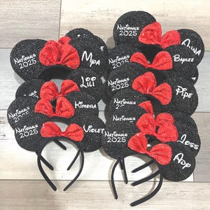May include: Nine black mouse ear headbands with red bows and white text. The text on the headbands reads "Nationals 2025", "Mpa", "Loo Lili", "Kimora", "Violet", "Aina Baplee", "Pipe", "Loss", and "App".