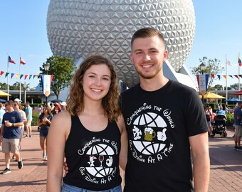 Peut inclure: Un couple porte des hauts noirs assortis avec l'inscription "Conquering the World One Drink At A Time" et un motif de globe. Le motif comprend une chope de bière, un verre de vin et des mains de Mickey Mouse. En arrière-plan, une grande sphère argentée et des drapeaux.