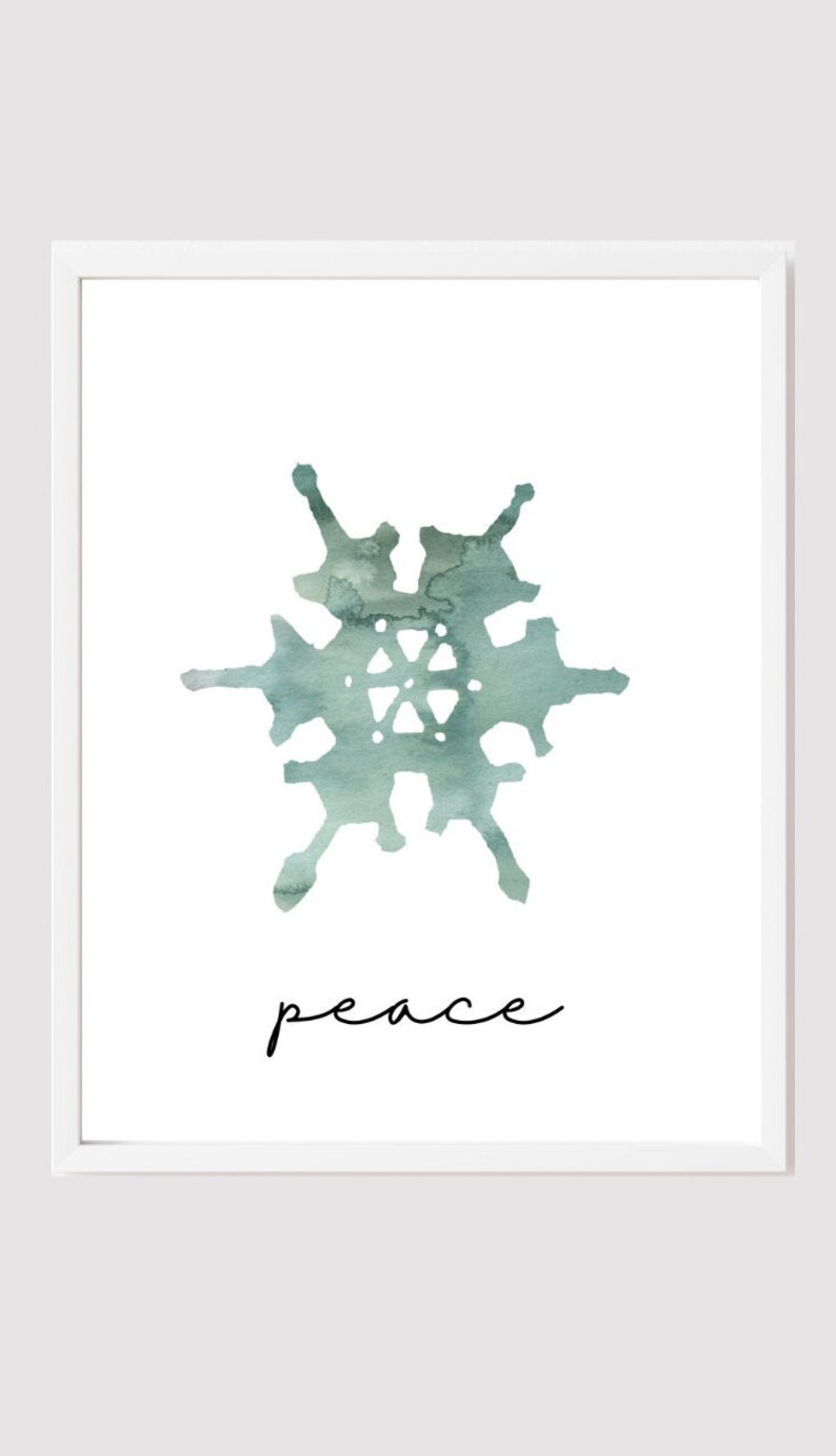 Pu&ograve; includere: Una stampa incorniciata bianca con un disegno ad acquerello di un fiocco di neve in tonalit&agrave; di blu e verde. La parola "pace" &egrave; scritta in corsivo nero sotto il fiocco di neve.