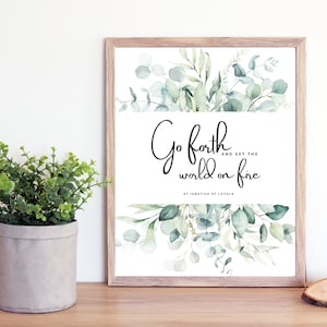 Puede incluir: Una impresión enmarcada con una ilustración de acuarela de hojas de eucalipto y la cita "Ve adelante y prende fuego al mundo" atribuida a San Ignacio de Loyola.