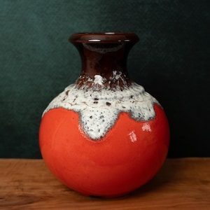 May include: A red and white ceramic vase with a brown rim. The vase has a round body and a smooth, glossy finish.