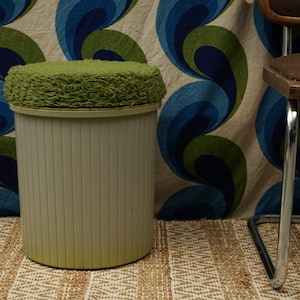 Peut inclure: Une poubelle cylindrique verte et blanche avec un couvercle en fourrure verte. La poubelle est posée sur un tapis à motifs brun et blanc devant un mur à motifs bleus et verts.
