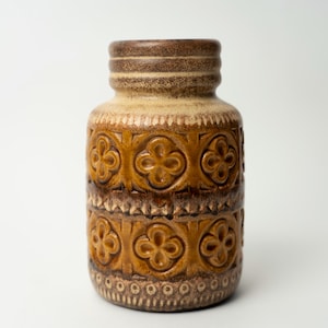 Può includere: Un vaso in ceramica marrone e crema con un motivo floreale. Il vaso ha un'ampia apertura e una base stretta.