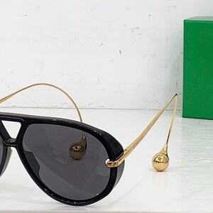 May include: Black aviator sunglasses with gold-tone metal arms and a distinctive bridge. The sunglasses have dark lenses and a rounded shape. A green box is in the background.