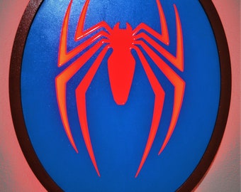 May include: A red spider-man logo on a blue background in a circular wooden frame. The logo is illuminated with red light.