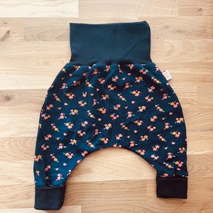 May include: Dark blue baby pants with a floral print featuring small pink, orange, and yellow flowers. The pants have a wide elastic waistband and cuffed legs.