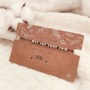 Peut inclure: Un bracelet noir avec des perles noires et argentées alternées, présenté sur une carte marron avec le mot "FRERE" et la phrase "WITH LOVE". La carte est ornée d'illustrations florales.
