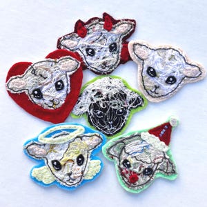 May include: A collection of embroidered lamb-shaped patches. Each patch features a lamb face with black eyes and is surrounded by different colored felt shapes, including red hearts, green, and blue. Some have festive accessories.
