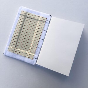 May include: Open journal with a white felt cover and a floral patterned interior. The interior fabric features a cream background with small red roses and green leaves. The right page is blank.