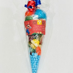 May include: A clear plastic cone filled with colourful sweets, tied with red and blue ribbon. A printed label with a cartoon character and the text "Thank you for coming to Teddy's 7th Birthday Party!" is attached to the cone.