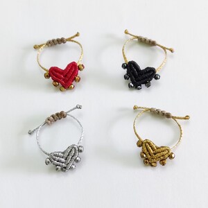 Puede incluir: Cuatro pulseras de amistad en forma de corazón con cuentas de diferentes colores. Las pulseras están hechas con un cordón anudado y tienen un dije en forma de corazón en el centro. Los colores de las pulseras son rojo, negro, plateado y dorado.
