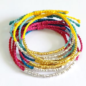 May include: A stack of colorful bracelets with silver and gold beads. The bracelets are made of braided string in shades of yellow, teal, and pink.