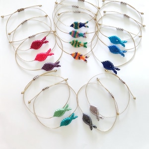 May include: A set of 10 colorful fish-shaped bracelets made with knotted string. Each bracelet has a different color and pattern, including blue, green, red, purple, and orange.