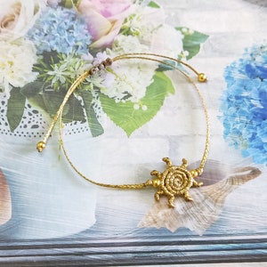 Pode incluir: Um bracelete de cordão dourado com um fecho de sol dourado. O bracelete é ajustável e tem um design simples.