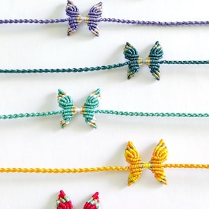 May include: Six colorful friendship bracelets with butterfly knots. The bracelets are made with different colored cords and feature gold accents.