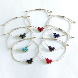 Può includere: Set di otto braccialetti dell'amicizia con ciondoli a forma di cuore in vari colori, tra cui rosso, blu, verde e nero. Ogni braccialetto è realizzato con un cordoncino sottile color oro e presenta piccole perline dorate.