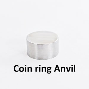 Puede incluir: Un yunque de metal plateado para anillos de monedas. El yunque es un pequeño cilindro redondo.