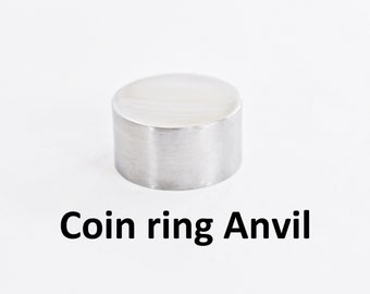 May include: A silver metal coin ring anvil. The anvil is a small, round cylinder.