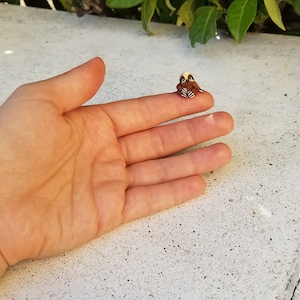 May include: A small, brown and white sloth figurine with black eyes, sitting on a finger.