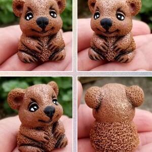 May include: A small, brown, textured figurine of a quokka with large, dark, glossy eyes, a black nose, and a smiling expression. The figure has rounded ears and a detailed, porous surface texture, shown from multiple angles in a four-part grid.