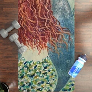 Könnte beinhalten: Eine Yogamatte mit einer farbenfrohen Illustration einer Meerjungfrau mit wallendem roten Haar und einem blauen Schwanz. Die Meerjungfrau trägt ein grün-blaues gemustertes Oberteil.