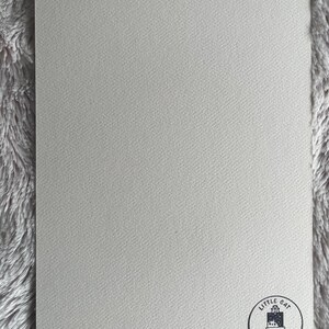 Op de afbeelding: Een blanco witte kaart met een zwart-wit logo in de rechterbenedenhoek. Het logo is een cirkel met de tekst "Little Cat Canvas" en een klein beeld van een ezel.