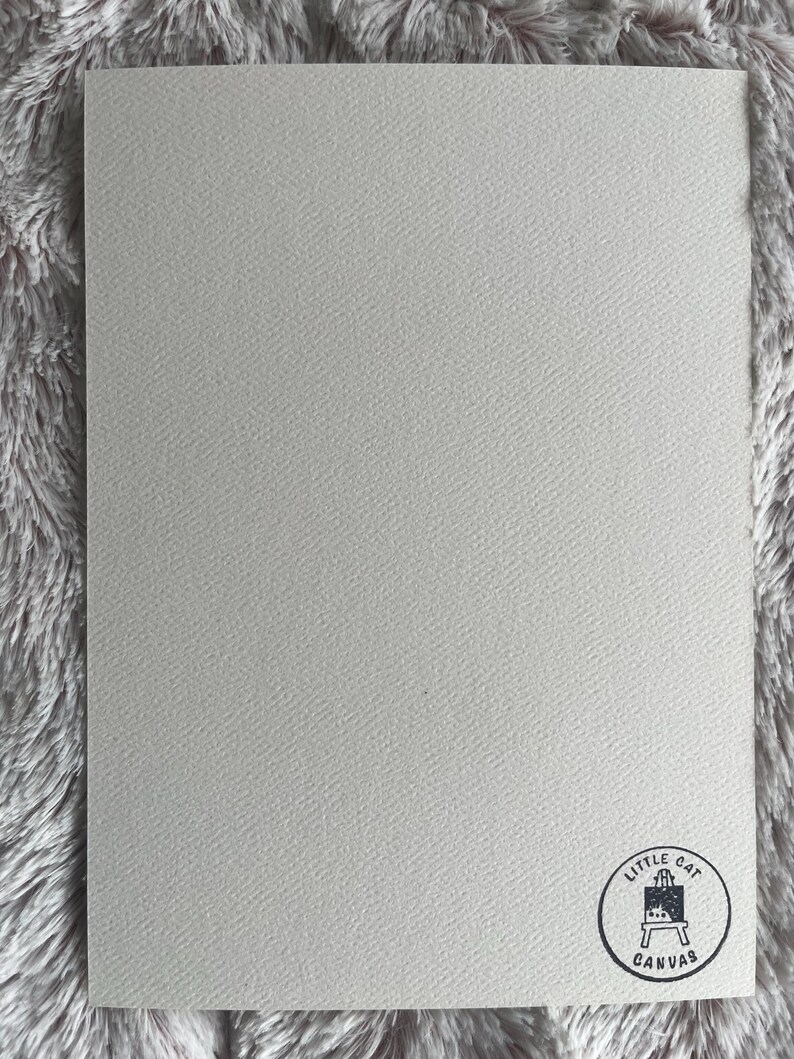 Op de afbeelding: Een blanco witte kaart met een zwart-wit logo in de rechterbenedenhoek. Het logo is een cirkel met de tekst "Little Cat Canvas" en een klein beeld van een ezel.