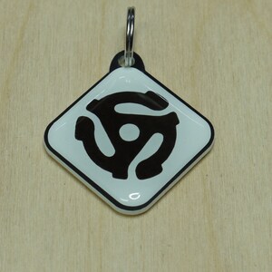 Peut inclure: Un porte-clés en forme de diamant blanc avec un symbole de disque vinyle noir.