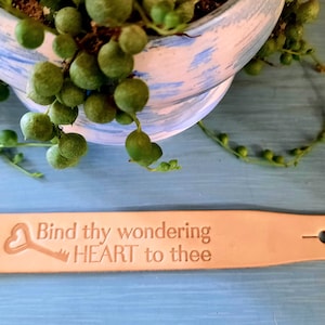 May include: A light brown leather bracelet with a heart and key design and the text "Bind thy wondering HEART to thee".
