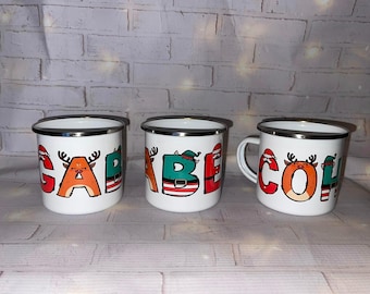 May include: Three white enamel mugs with silver rims. Each mug features a different letter of the name "GABEH COH" in a festive Christmas design. The letters are decorated with reindeer, Santa hats, and elf hats.