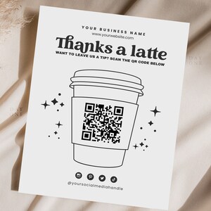 May include: Black and white illustration of a coffee cup with a QR code on the side. The text "Thanks a latte" is above the cup and "WANT TO LEAVE US A TIP? SCAN THE QR CODE BELOW" is below the cup. Social media icons are below the text.