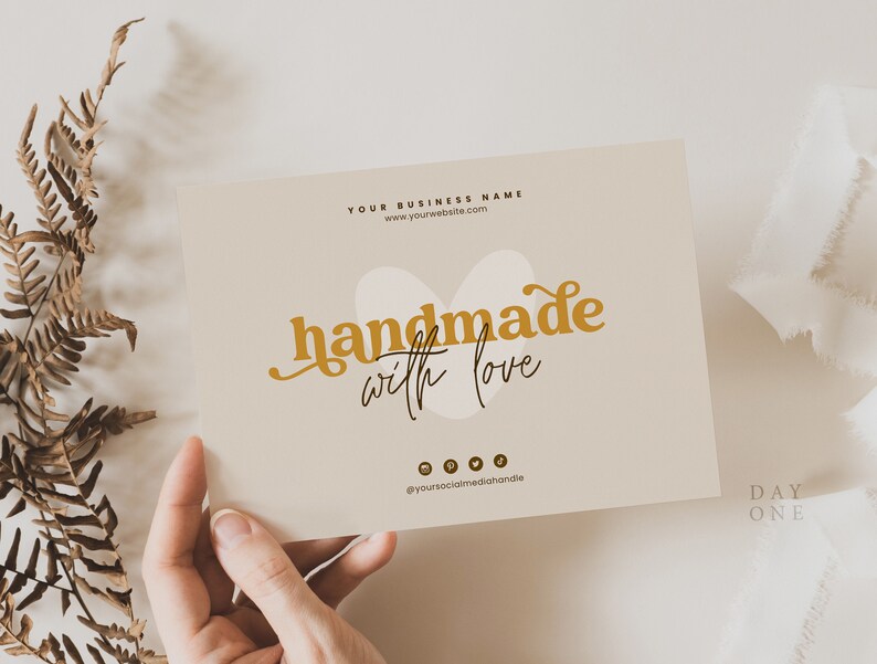 Op de afbeelding: Een beige kaart met de tekst "YOUR BUSINESS NAME" en een websiteadres. De kaart bevat ook de tekst "handmade with love" in gouden kleur met een gestileerde hartvorm achter de tekst. Op de onderkant van de kaart staan ​​social media-pictogrammen.
