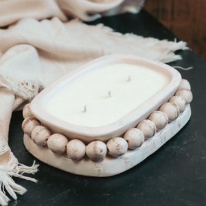 May include: White ceramic candle holder with a three-wick candle and a decorative beaded trim.