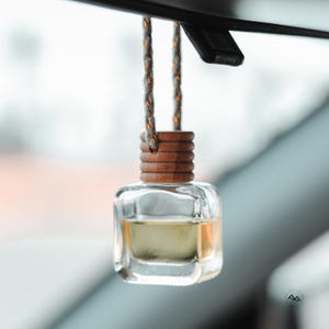 May include: A clear glass bottle with a wooden cap hangs from a white string. The bottle is filled with a light yellow liquid and is a car air freshener.