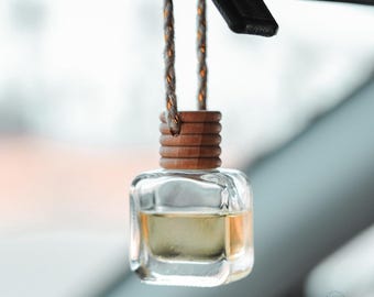 May include: A clear glass bottle with a wooden cap hangs from a white string. The bottle is filled with a light yellow liquid and is a car air freshener.