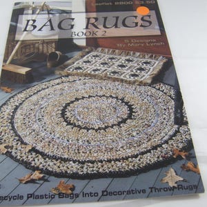 May include: A book cover titled "BAG RUGS BOOK 2" featuring a circular rug made from recycled plastic bags. The cover also shows a square rug and the text "Recycle Plastic Bags Into Decorative Throw Rugs."