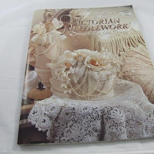 Puede incluir: Un libro titulado "Victorian Needlework Designs for Our Times" de Annie Potter. La portada presenta una imagen detallada de un sombrero cubierto de encaje con una muñeca y detalles florales, y otros artículos de encaje y tela.
