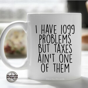 May include: White ceramic coffee mug with black text that reads "I have 1099 problems but taxes ain't one of them".