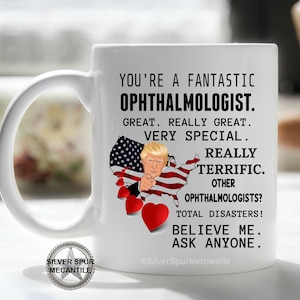 Pu&ograve; includere: Una tazza da caff&egrave; in ceramica bianca con un messaggio divertente sugli oculisti. La tazza presenta un'immagine di cartone animato di Donald Trump che punta verso lo spettatore con un cuore rosso e una bandiera americana sullo sfondo. Il testo dice: "Sei un fantastico oculista. Grandioso. Davvero grandioso. Molto speciale. Davvero fantastico. Altri oculisti? Disastri totali! Credimi. Chiedi a chiunque."