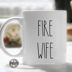 May include: White ceramic coffee mug with black text that reads "FIRE WIFE" and a small logo at the bottom that reads "Silver Spur Mercantile".