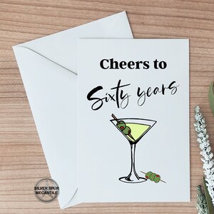 May include: A white card with black text that reads "Cheers to Sixty Years" and a drawing of a martini glass with olives.