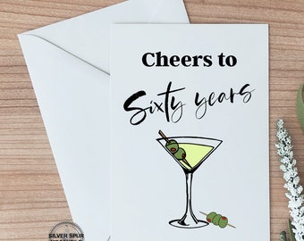 May include: A white card with black text that reads "Cheers to Sixty Years" and a drawing of a martini glass with olives.